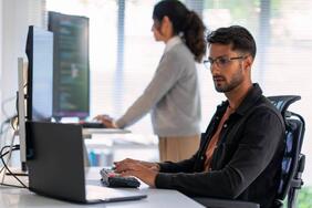 A cyber security analyst with eye glasses working on a laptop.