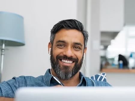 A smiling man with headphones using a laptop in a bright living room.