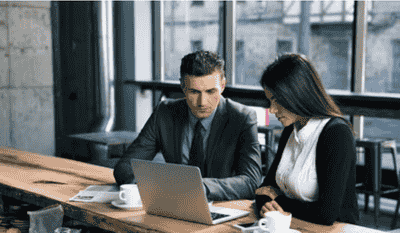 A man and woman in business attire working together on a laptop at a professional space.