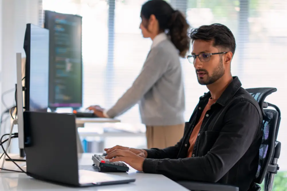 A cyber security analyst with eye glasses working on a laptop.