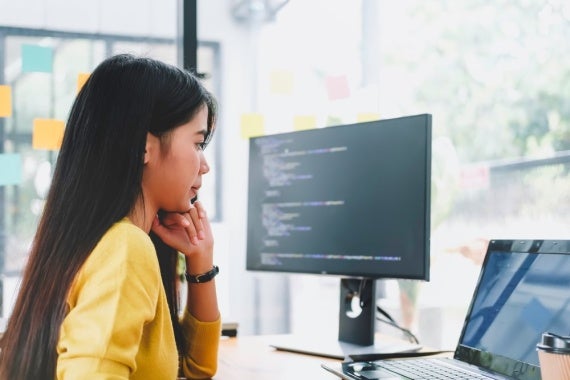 A data scientist studies code on a laptop and computer monitor.