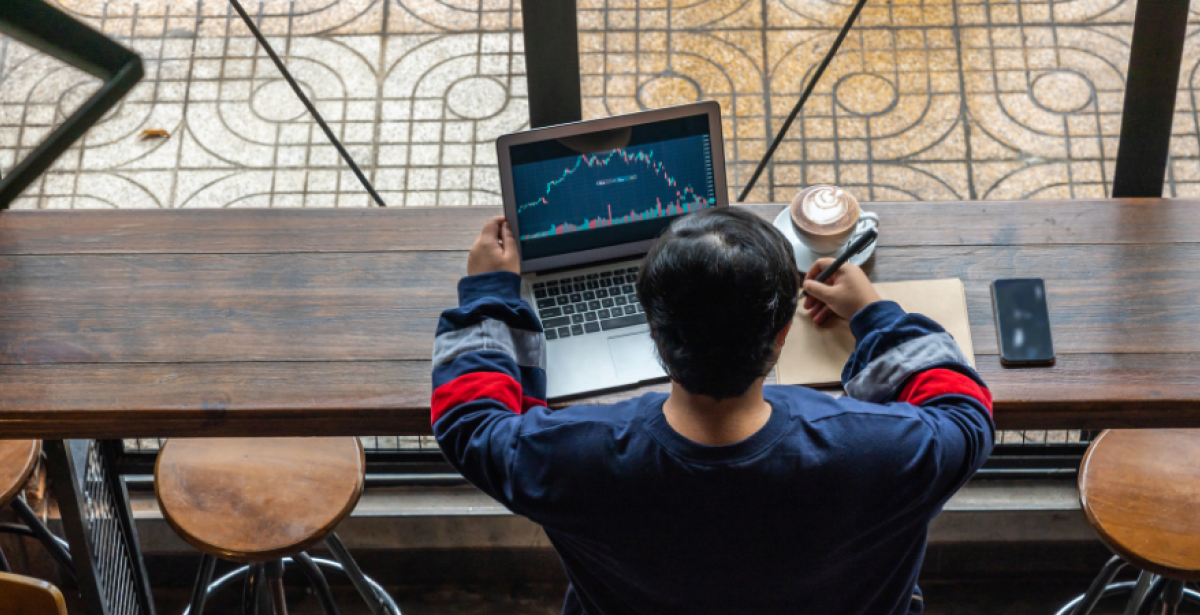 From above, a student sits with a coffee and his laptop researching fintech courses in Australia