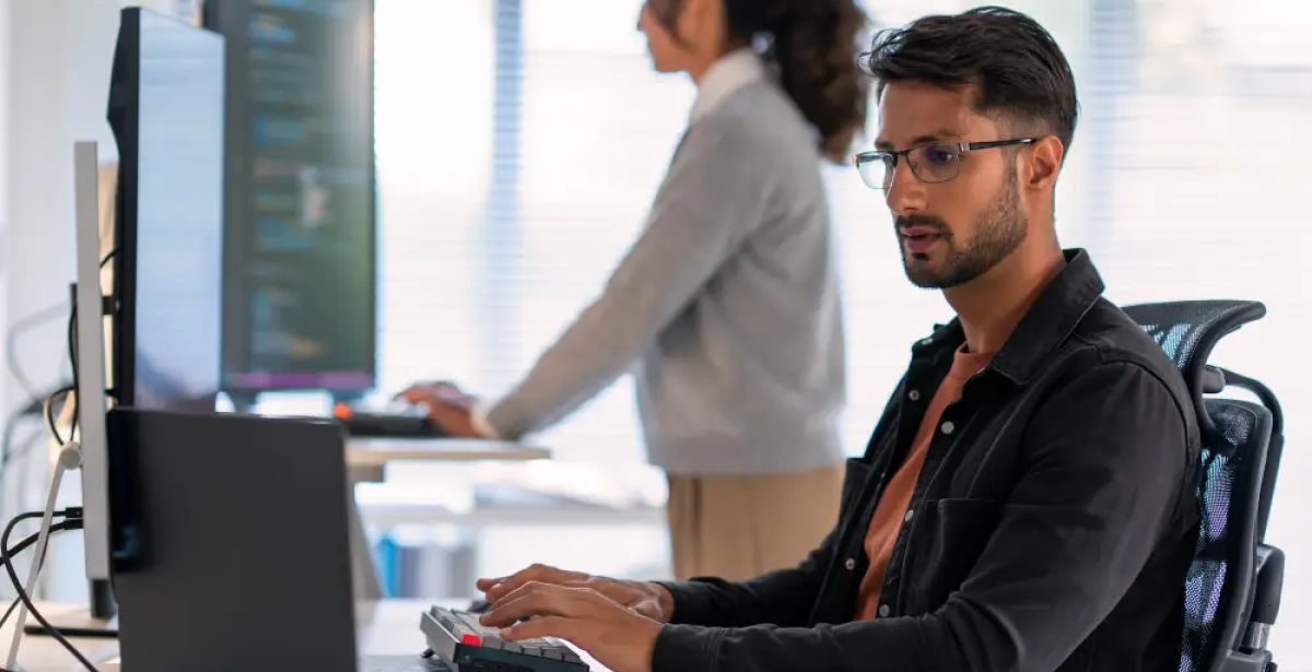 A cyber security analyst with eye glasses working on a laptop.