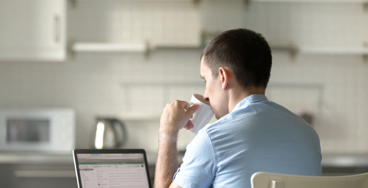 A university student sips coffee while studying at home.