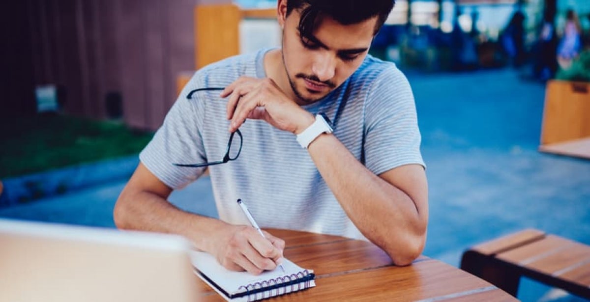 A postgraduate student writing revision notes in a notepad.