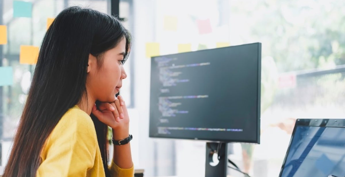 A data scientist studies code on a laptop and computer monitor.