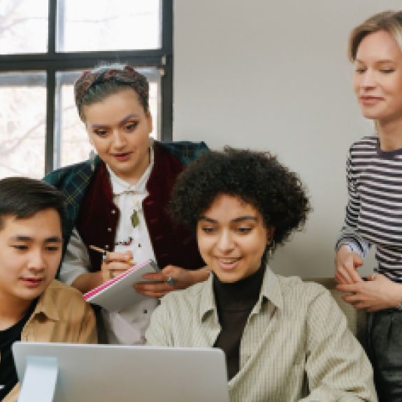 Postgraduate students huddled around a student with a laptop.