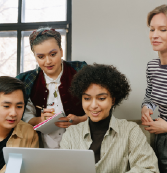 Postgraduate students huddled around a student with a laptop.