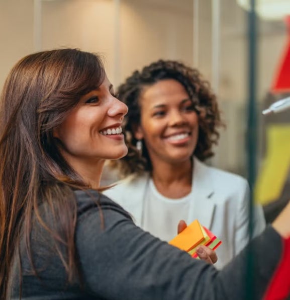 Two women smiling and collaborating while writing ideas on colorful sticky notes.