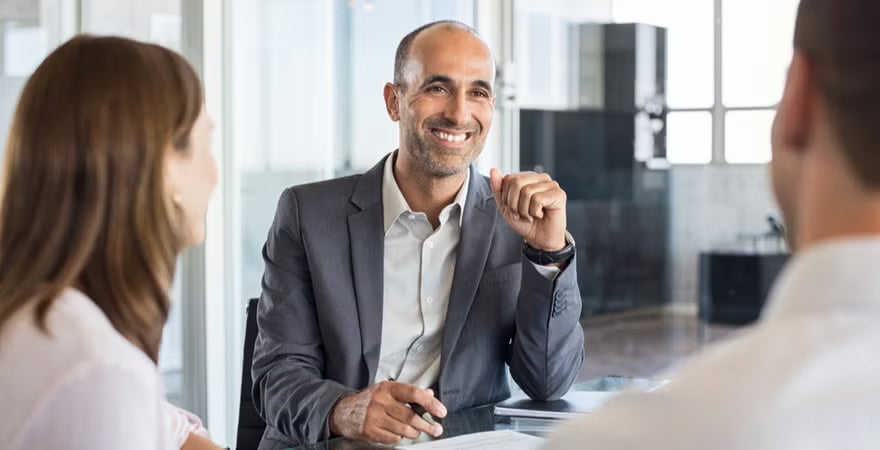 An analyst meets with two coworkers at a conference table.
