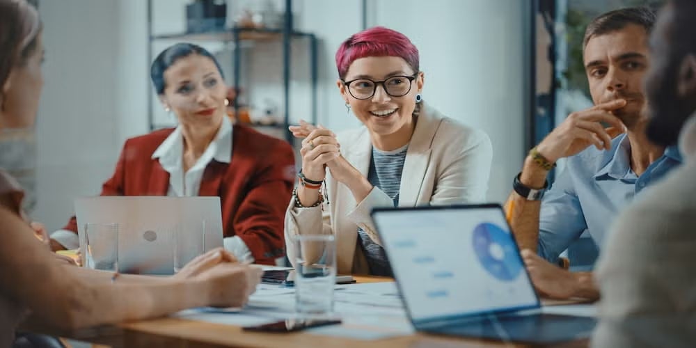 Group of diverse professionals in a meeting discussing data, with laptops and charts displayed, promoting inclusion and collaboration in cyber security.