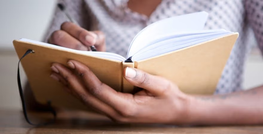 A woman is focused on writing in a notebook, capturing her thoughts with a pen in a cozy setting.