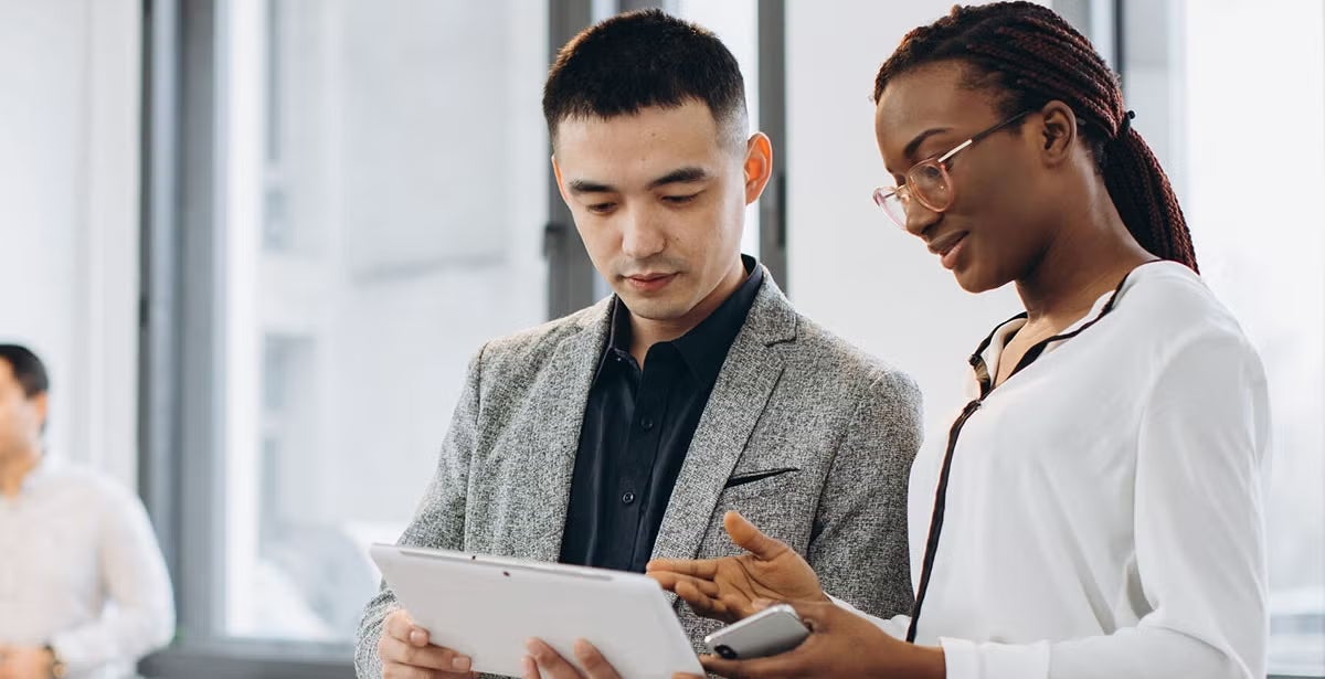 Two professionals, one man and one woman, review a tablet together in a bright office, illustrating discussion about cybersecurity and technology teamwork.