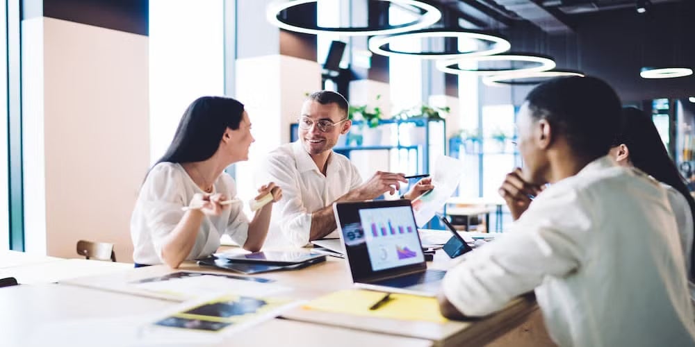 A group of business professionals engaged in a discussion during an office meeting around a conference table.